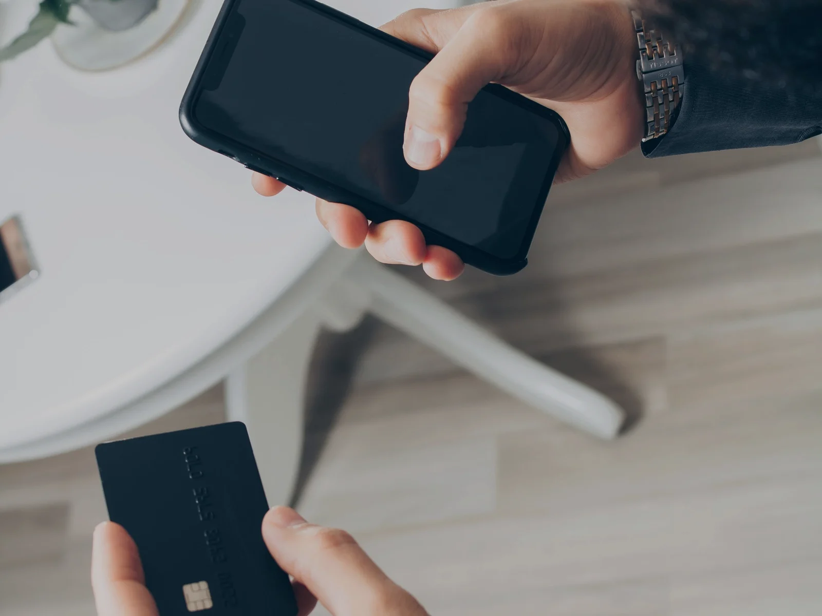 En person håller ett bankkort och en mobiltelefon för en digital betalning