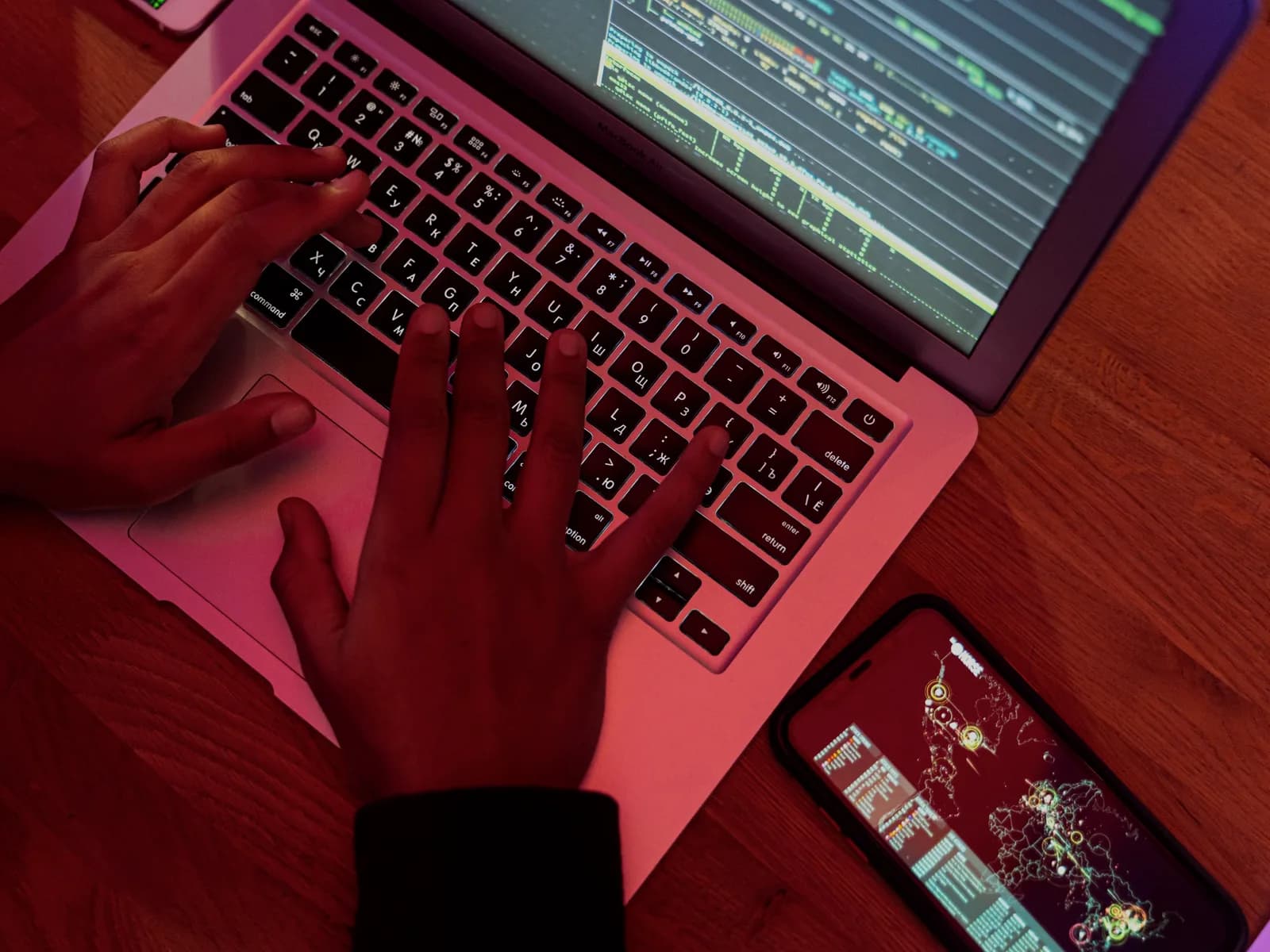Händer vid en laptop med programkod och en mobiltelefon, som symbol för wallet och smarta kontrakt