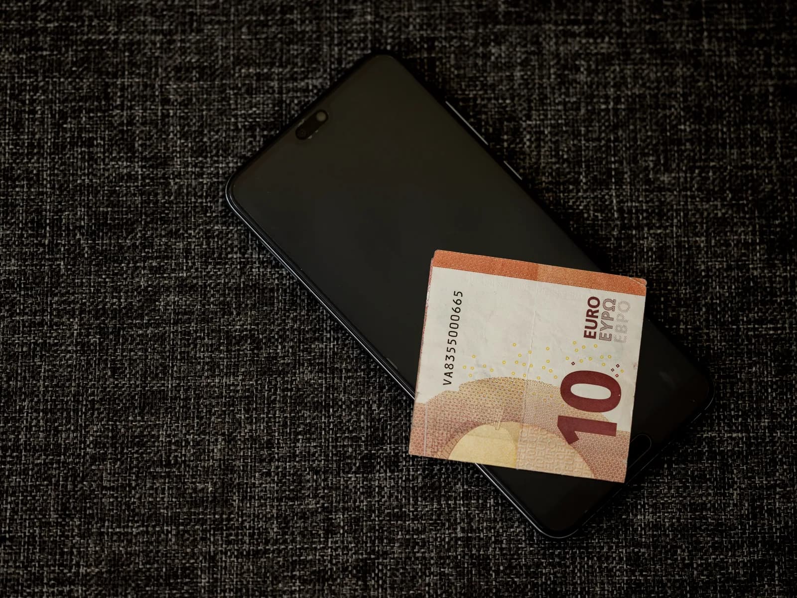 Eurosedel ovanpå en mobiltelefon mot mörk textil, som symbol för länken mellan fiatvaluta och digitala tokens
